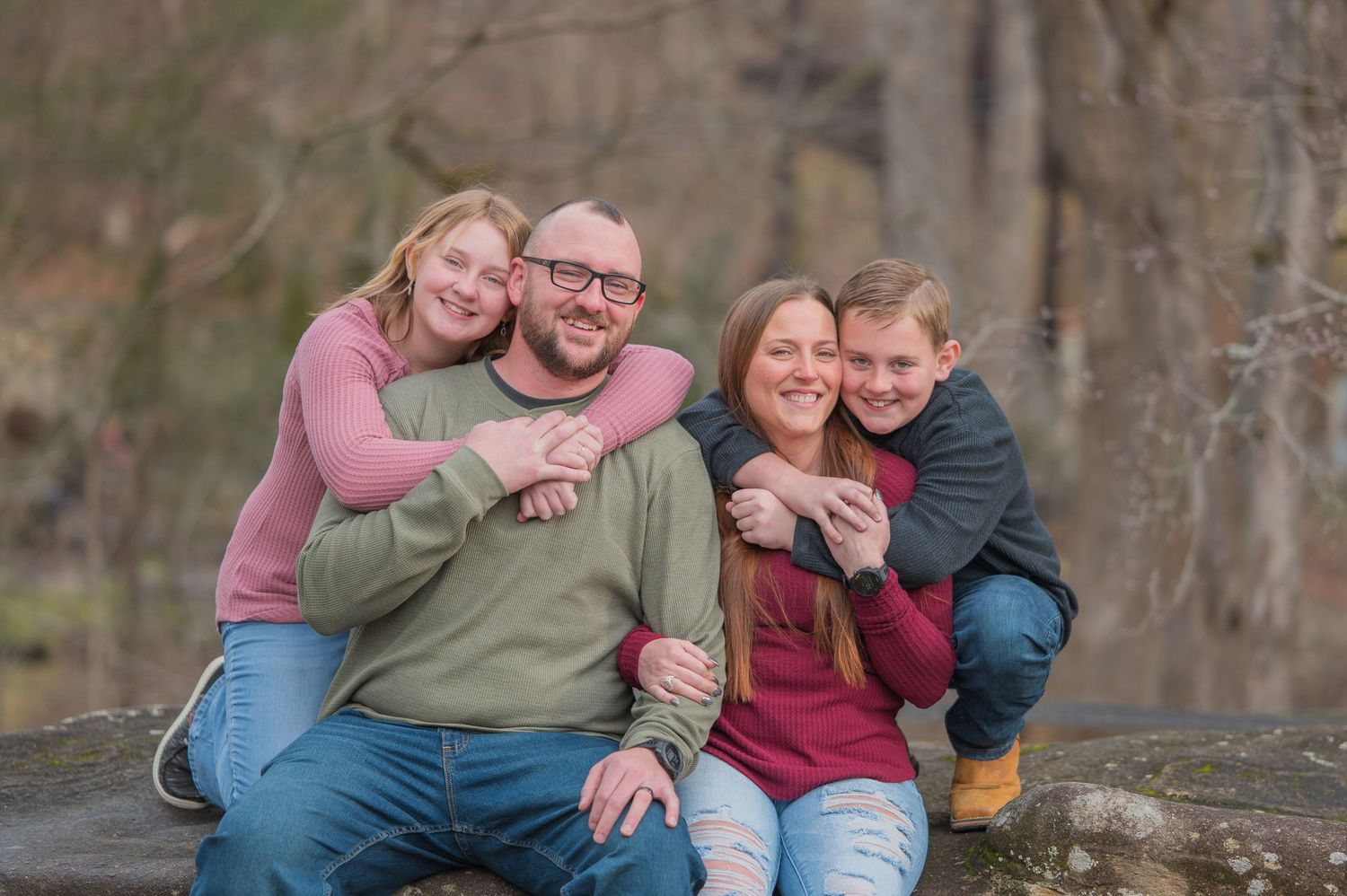 Happy family of four sitting together and embracing outdoors against a rocky cliff background in Sevierville TN.