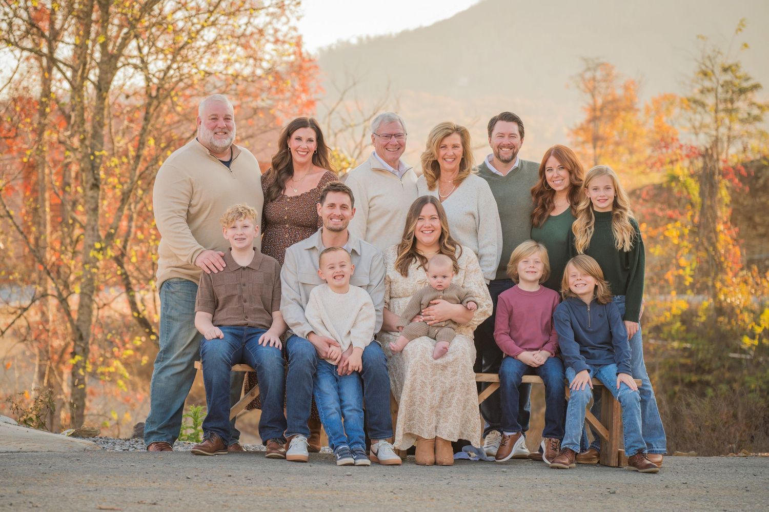 A large family group poses together outdoors against a backdrop of autumn foliage and mountains by Gatlinburg TN photographers.