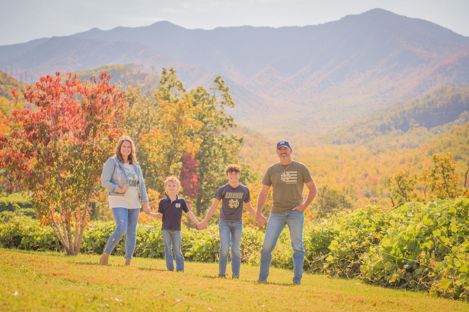 A family takes a portrait against a stunning backdrop of fall foliage and Great Smoky Mountains in autumn in Sevierville TN.