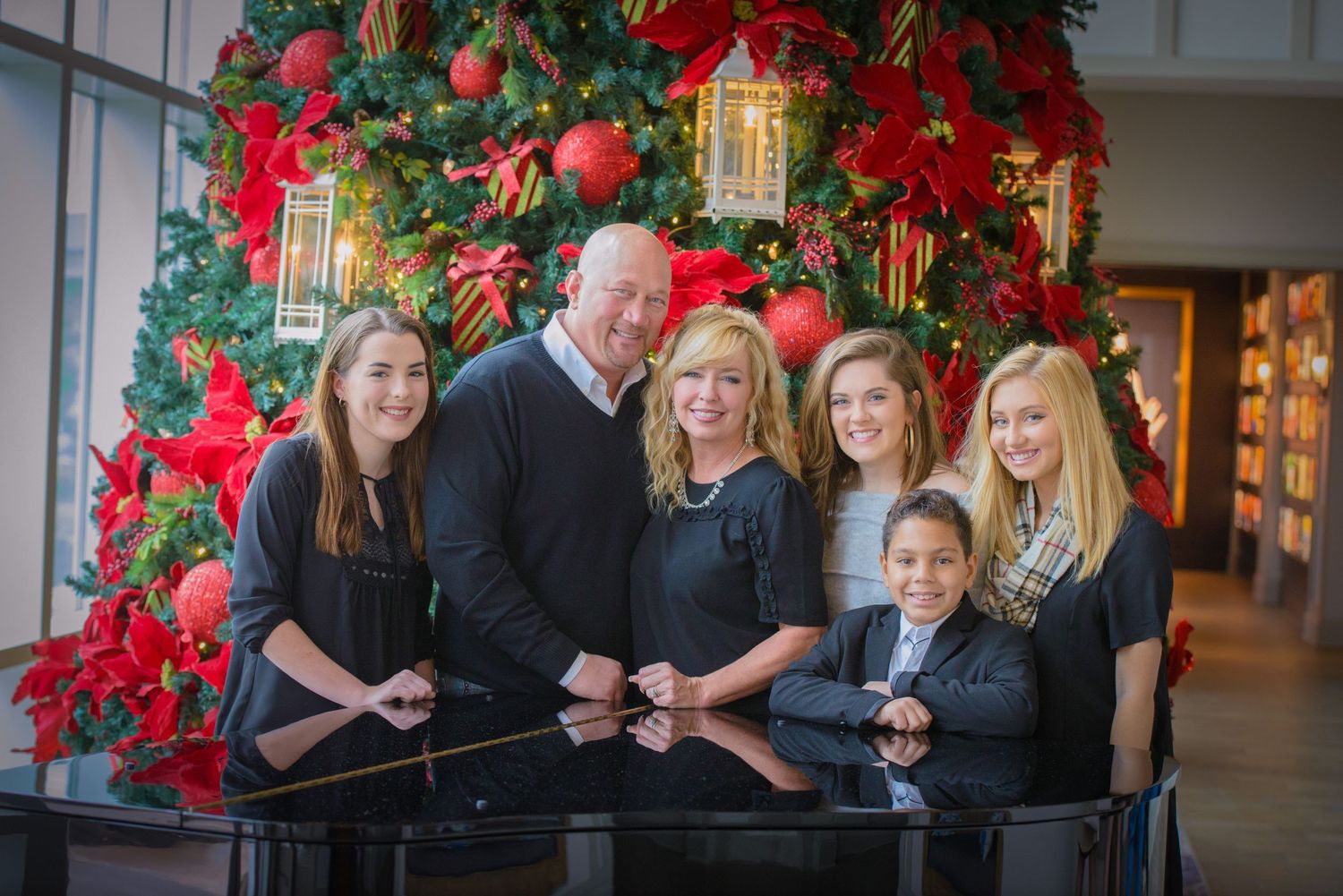 Family poses together at a piano with festive Christmas decorations and a red poinsettia decorated tree at Dollywood's DreamMore Resort.