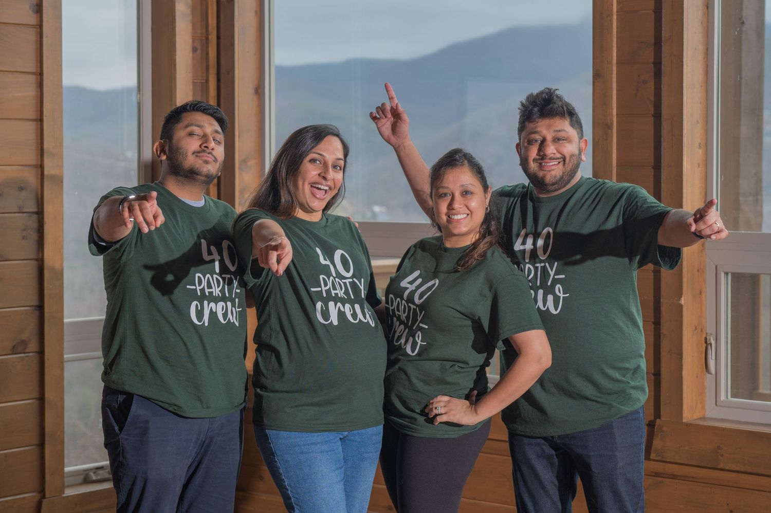 A group in matching t-shirts poses together near windows with mountain views in the background. Fun cabin family portraits in Gatlinburg TN.