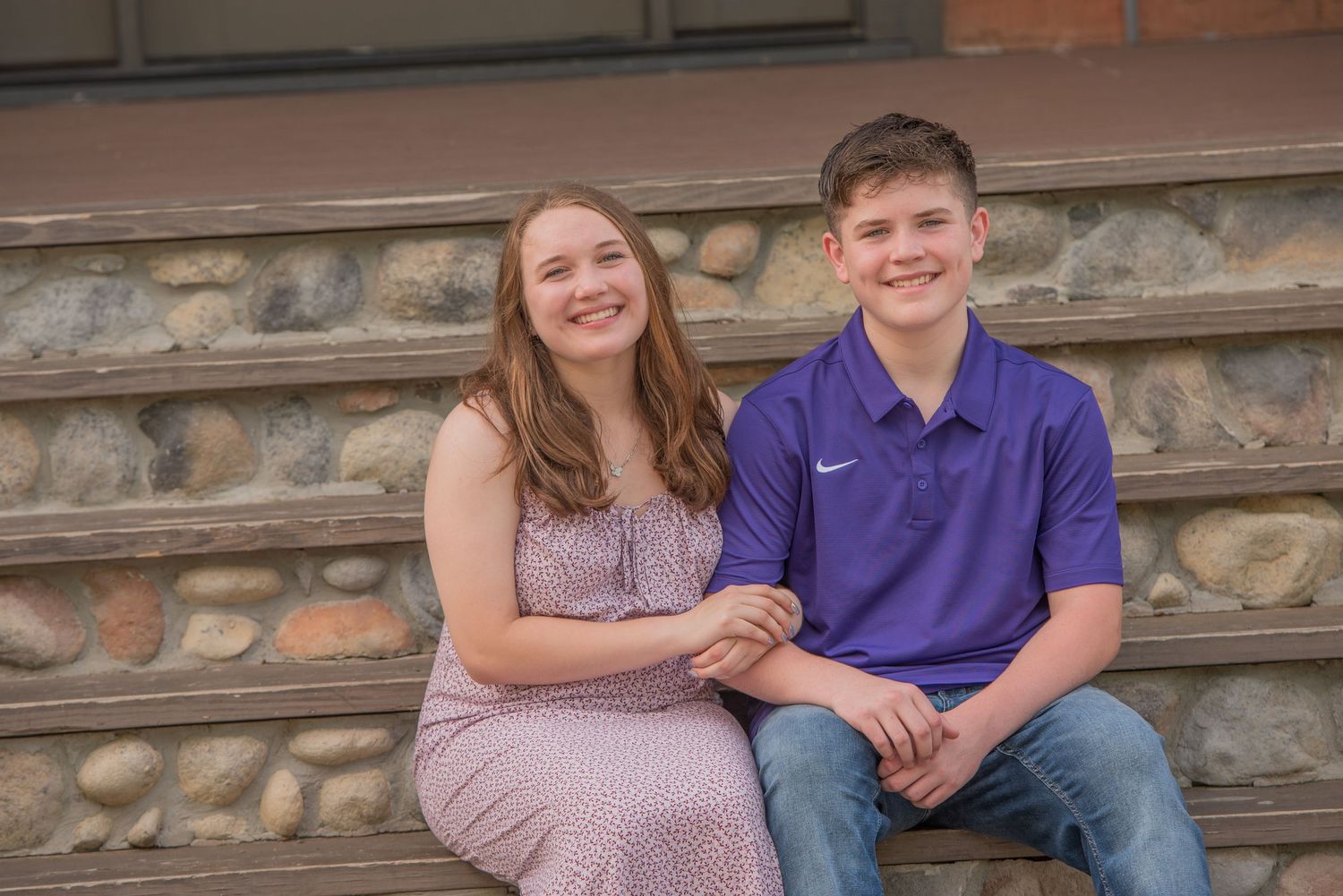 Brother and sisters sit together holding hands on stone steps during a casual outdoor photo session by Pigeon Forge Photographers.