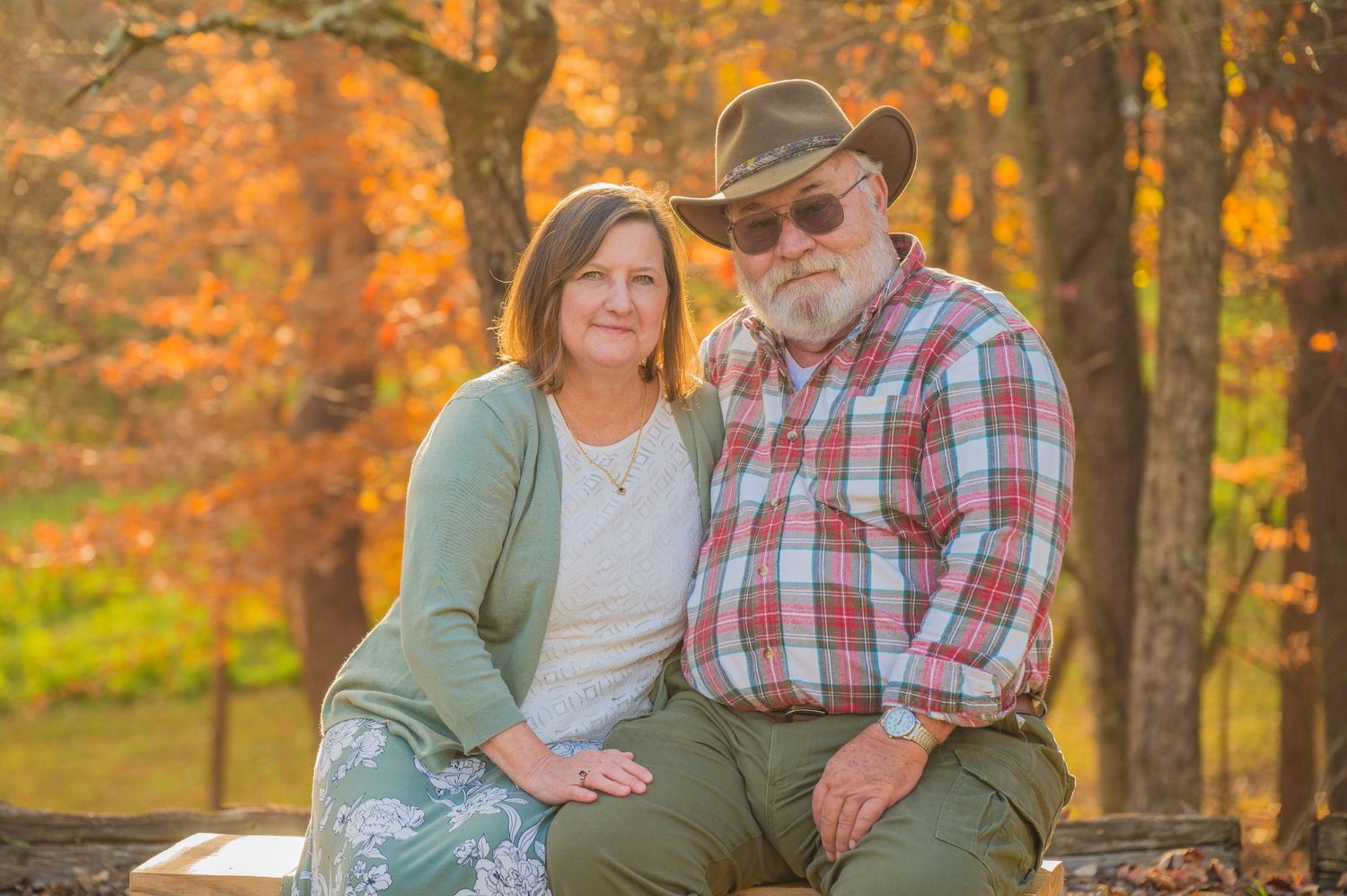A couple sits together on a bench surrounded by vibrant autumn foliage with golden light filtering through the trees in Sevierville TN.