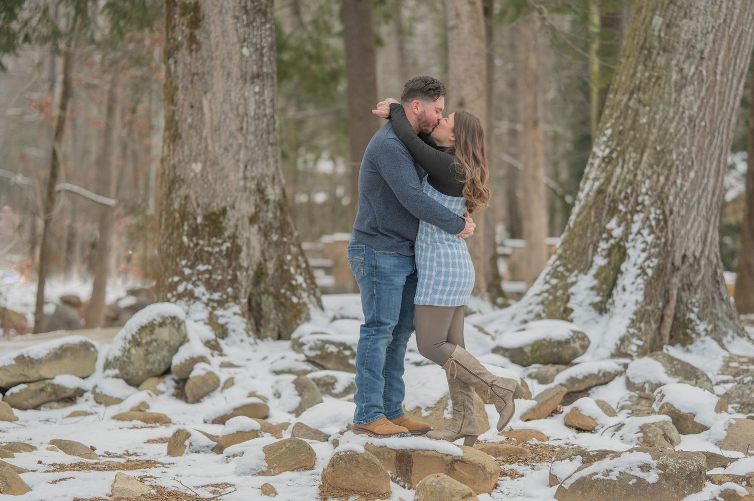 A couple embraces while standing on snow-covered rocks in a winter forest setting by gatlinburg tn engagement photographers.
