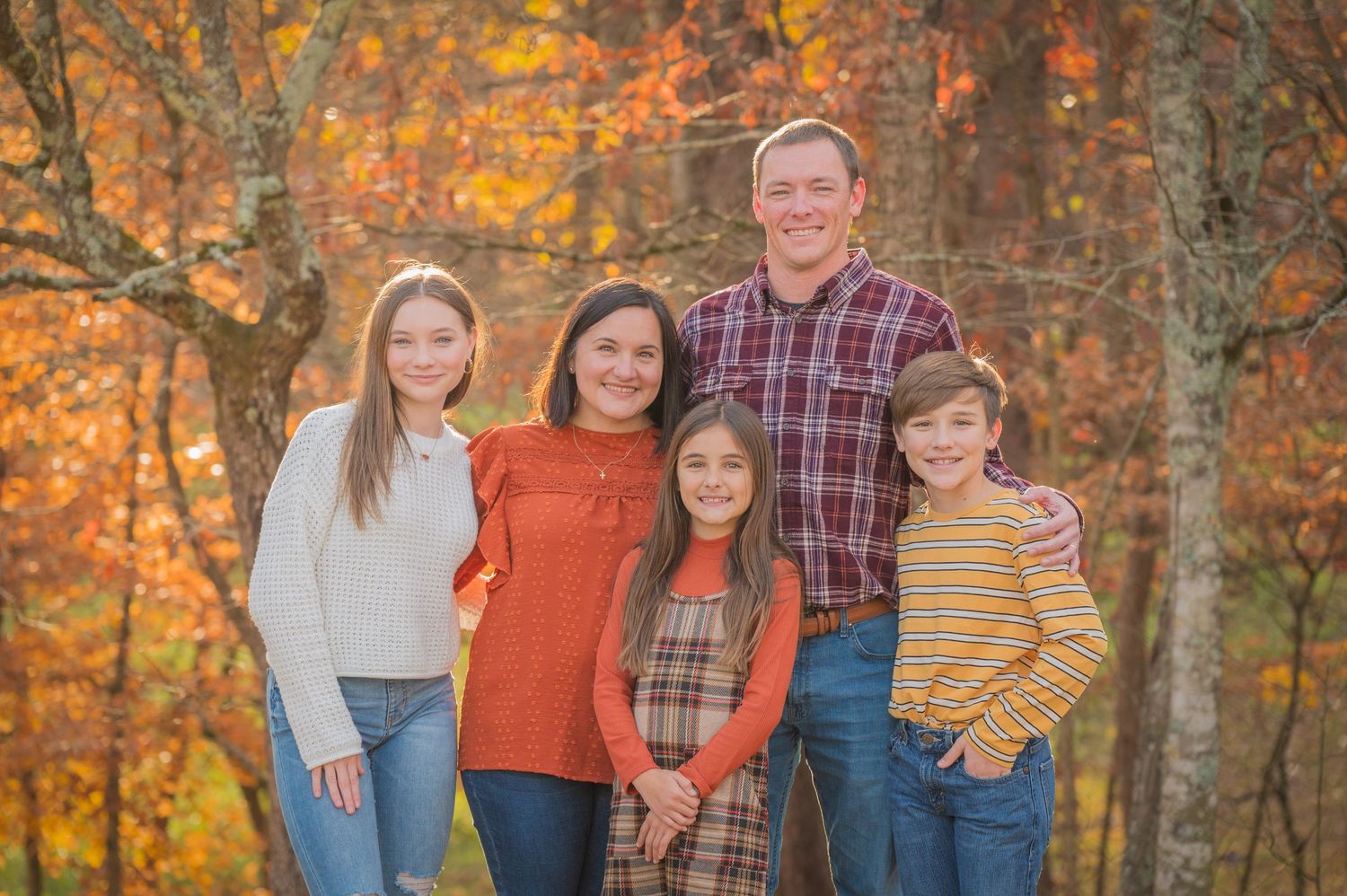 Gatlinburg TN Photographers portrait of a family stands together in a forest setting during autumn with golden foliage in the background.