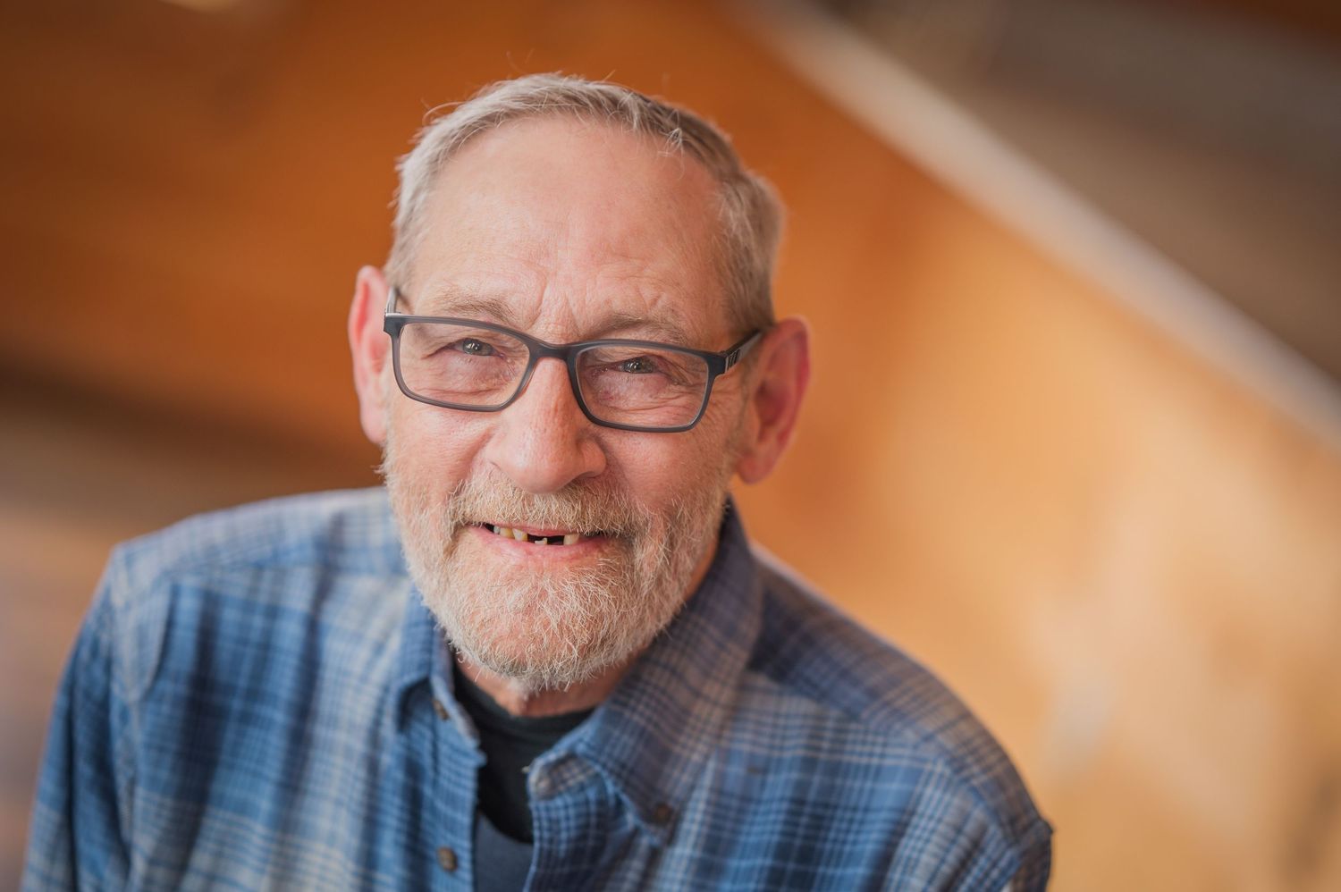 Smiling grandpa wearing glasses and a blue denim shirt against cabin background in casual portrait at Gatlinburg TN.