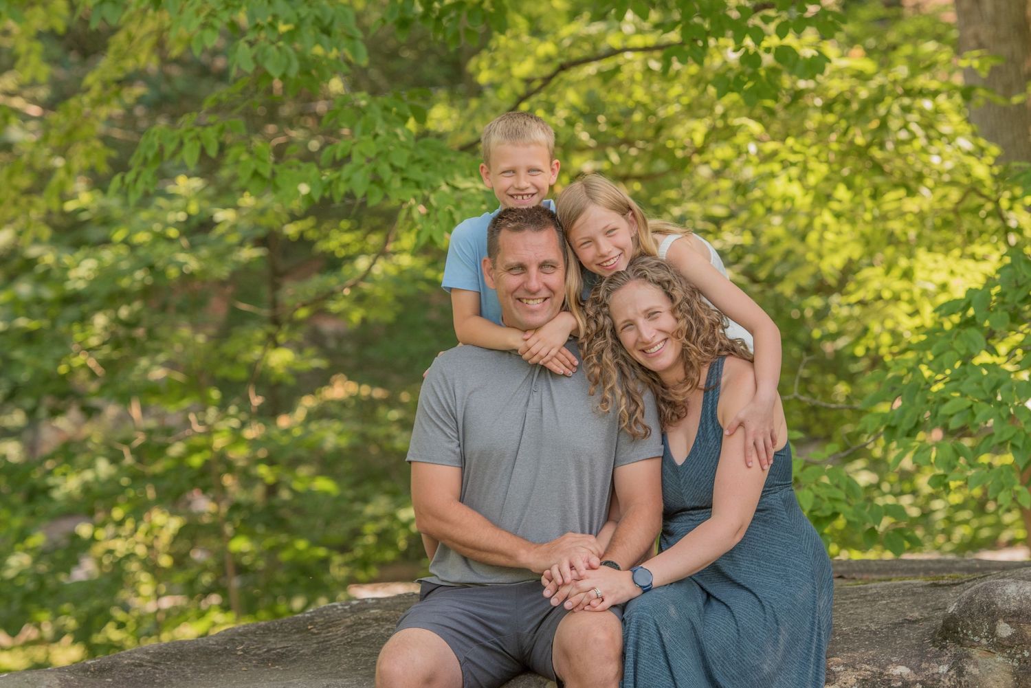 A family sits together on a wooden railing outdoors with lush green foliage in the background in Townsend TN.