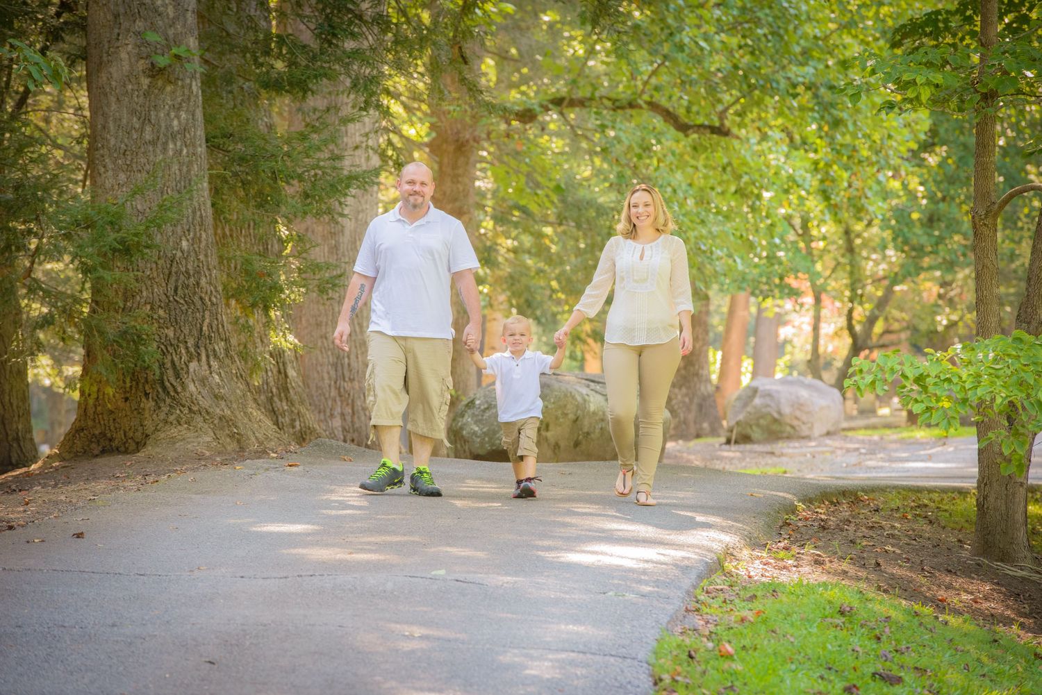 Pigeon Forge Photographer portrait of an outdoor family walking together holding hands on a sunlit park path surrounded by lush green trees.