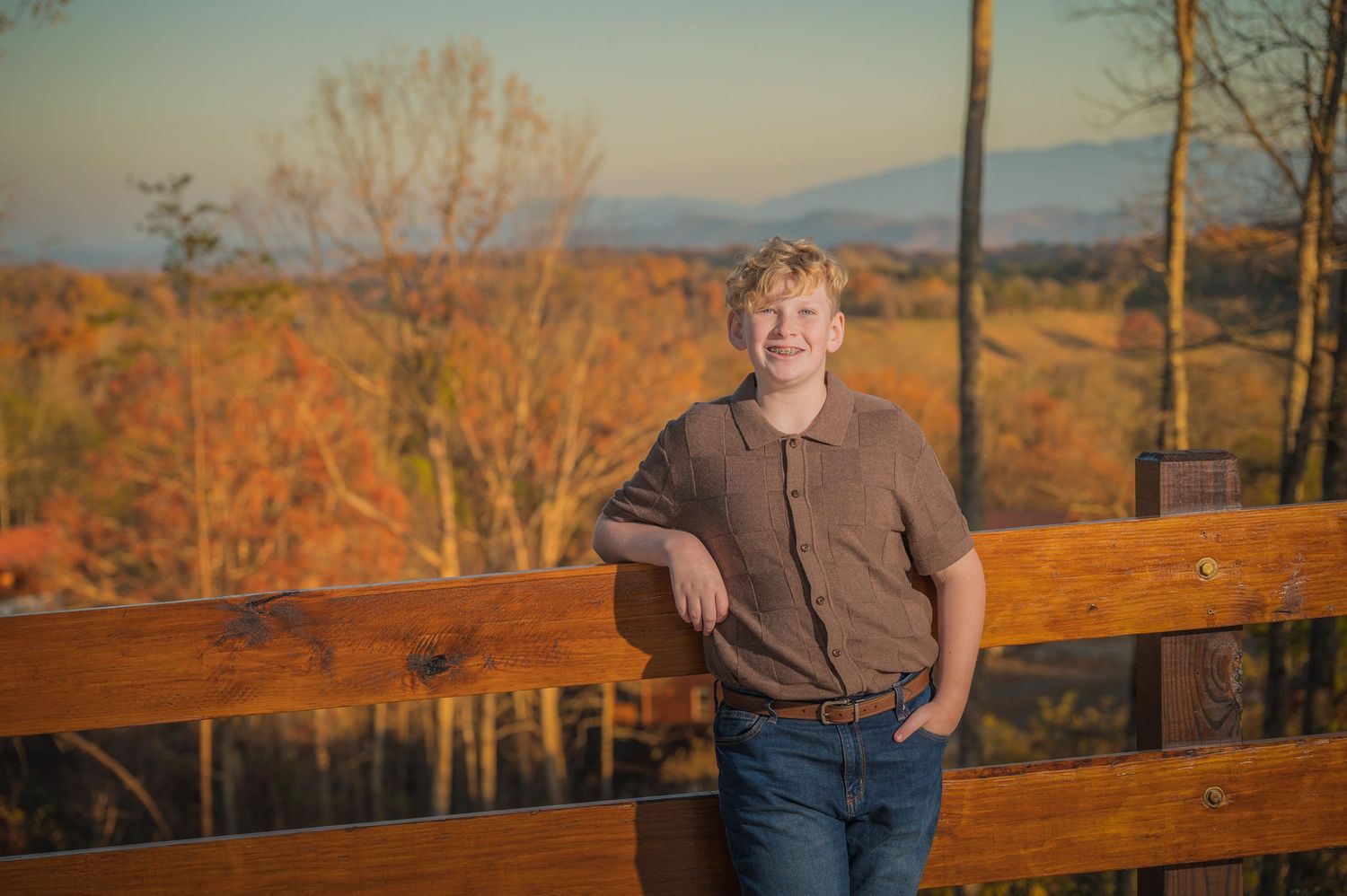 Young boy standing on wooden deck railing during sunset with autumn foliage and mountains in the background at Sevierville Tn Cabin Rental.