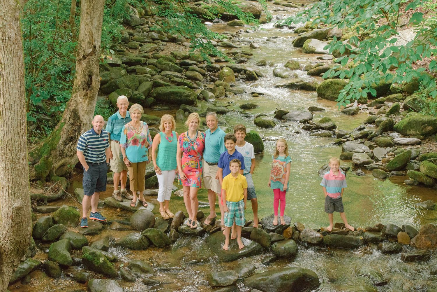 A group enjoys a summer day exploring a rocky creek bed surrounded by lush green forest and trees by Gatlinburg Photographer.