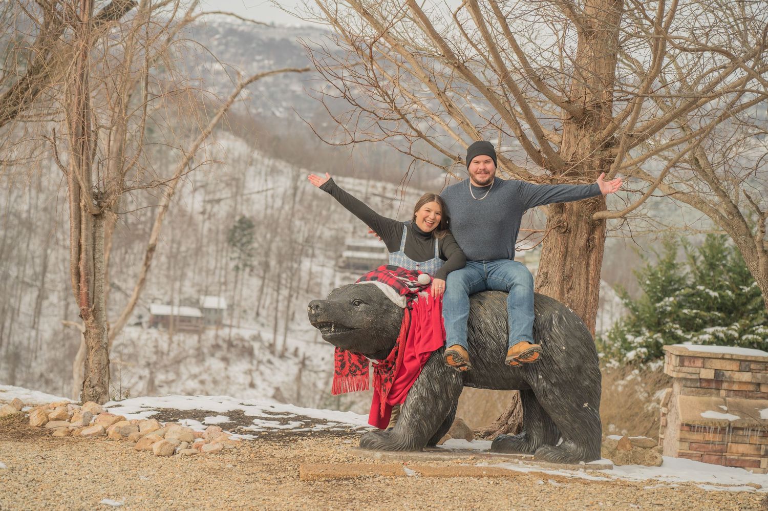 A couple poses on a red ATV in a winter mountain landscape with bare trees and snow-covered scenery in the background in Gatlinburg TN.
