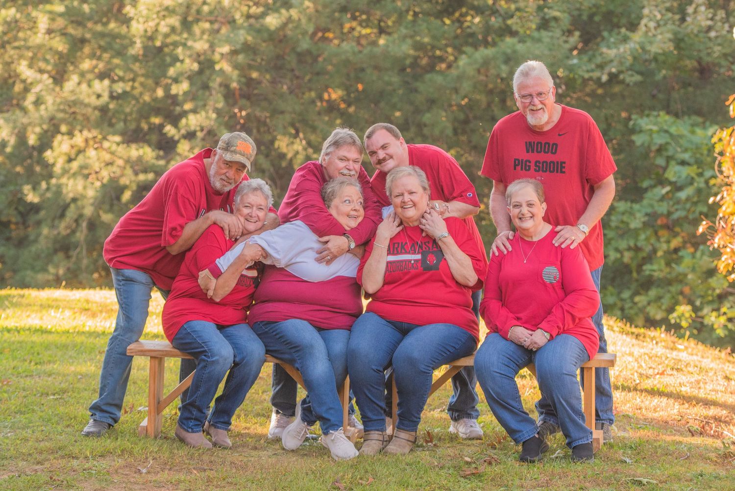 A family wearing matching red sweatshirts sits together on a wooden bench outdoors during autumn at their cabin rental in Sevierville TN.