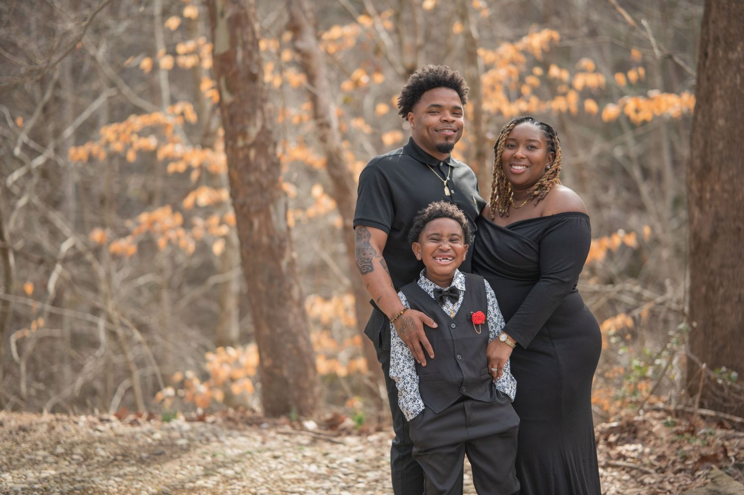 A family of three poses together outdoors in autumn, with golden fall foliage visible in the background in Sevierville TN.