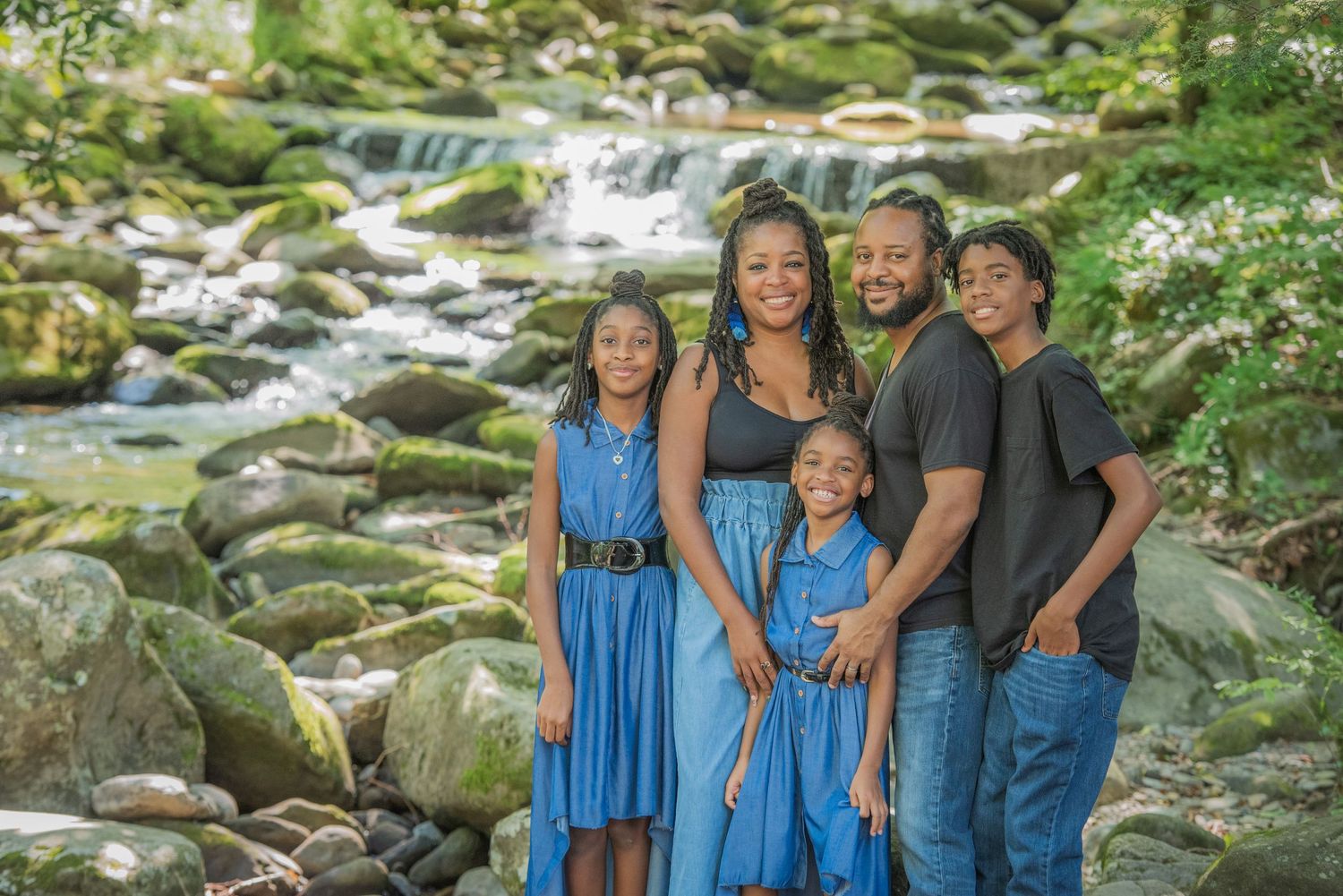 A family poses together by a cascading waterfall stream with mossy rocks and lush greenery in the background Gatlinburg TN.