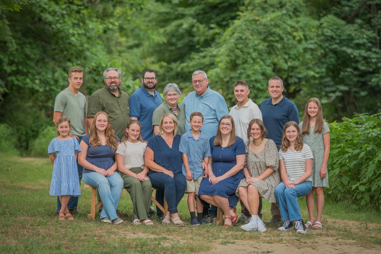 A large family wearing coordinated blue and neutral colors poses outdoors for a natural portrait by Gatlinburg Photographers TN.