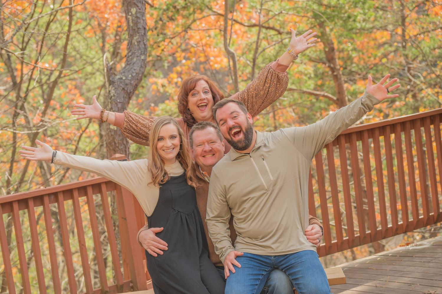 A group poses joyfully with outstretched arms at a cabin surrounded by vibrant autumn foliage in Sevierville TN