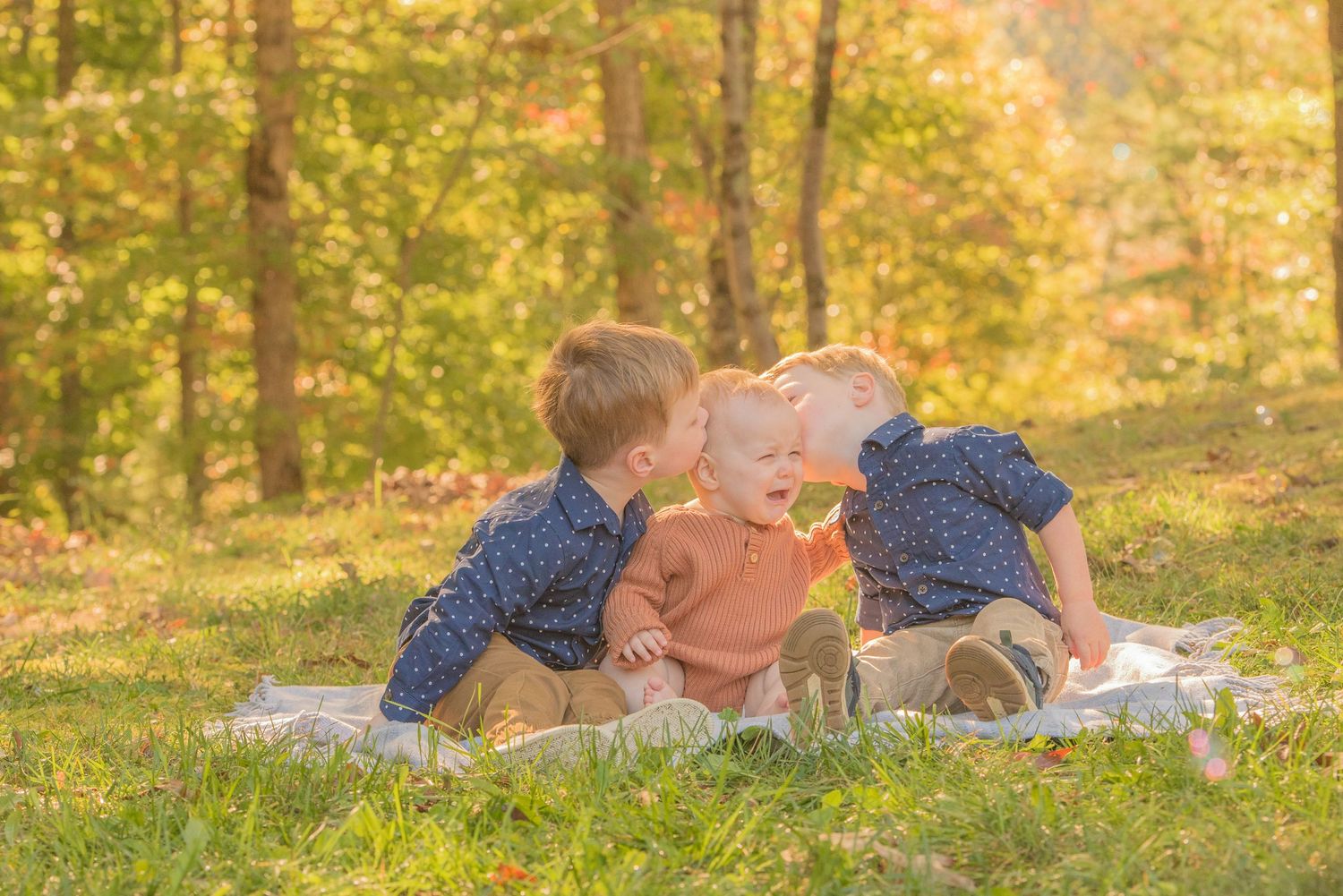 Pigeon Forge Photographer captures Children wearing polka dot clothing lay on a blanket in a sunny autumn forest setting during golden hour.
