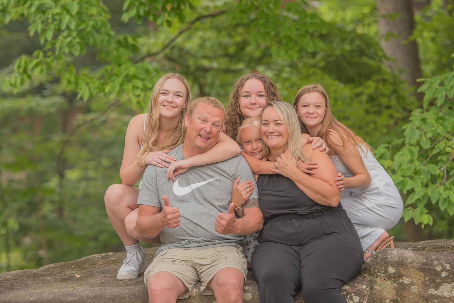 A family sits together outdoors on a rocky ledge surrounded by green foliage on a sunny summer day in Pigeon Forge TN.