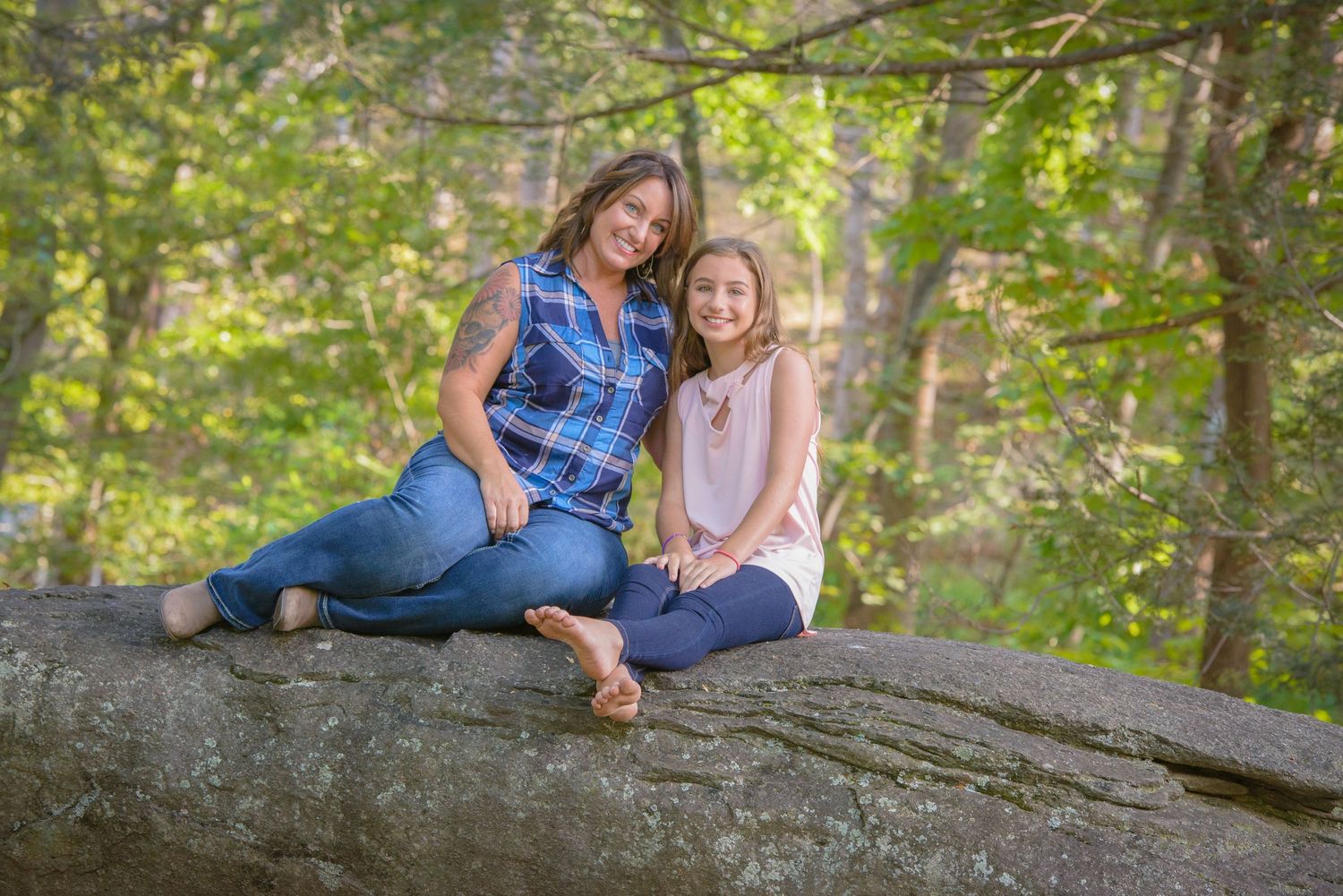 Mother and daughter in casual clothing sitting together on a large rock in a sunlit forest setting Pigeon Forge TN.