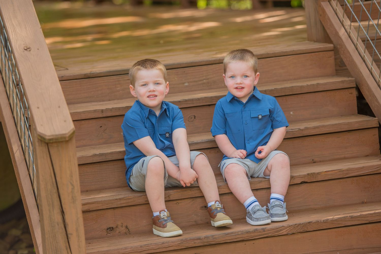 Two young children in matching blue polo shirts and khaki shorts sitting together on wooden outdoor steps in Pigeon Forge TN.
