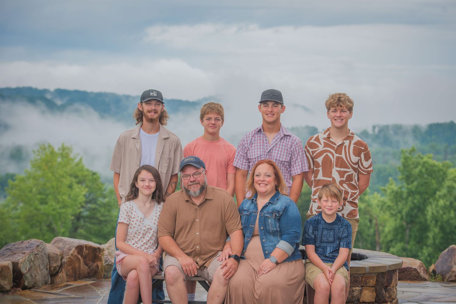 A family poses together on a rock overlook with misty mountains and green forest in the background Pigeon Forge TN.