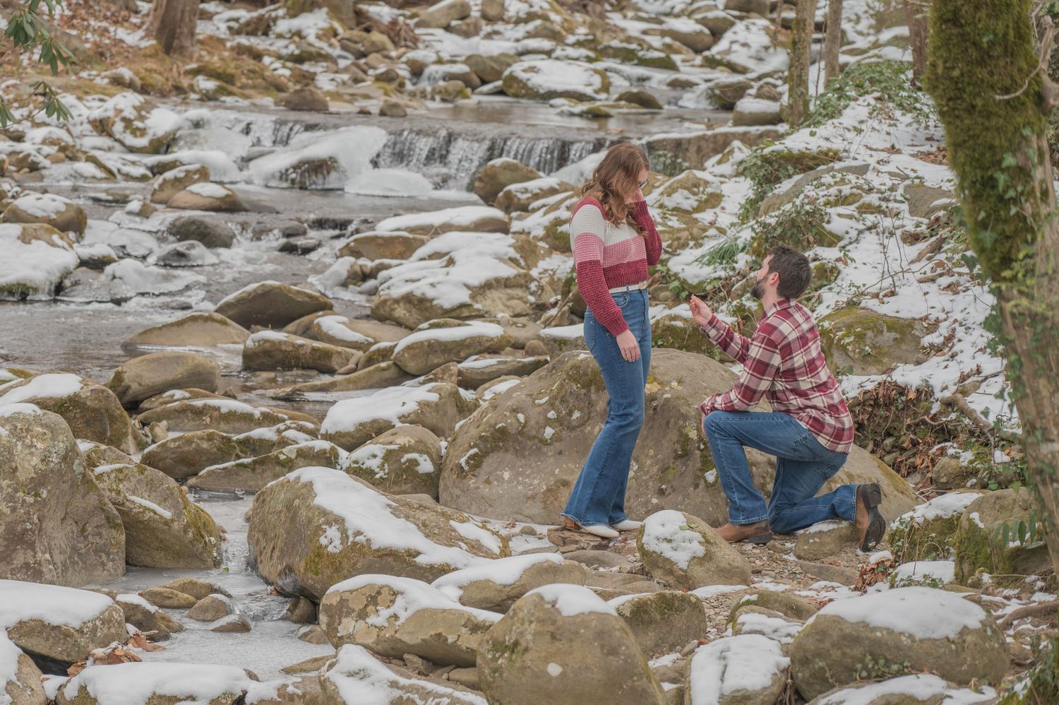 Two people pose for a proposal moment on snow-covered rocks along a winter mountain trail by Gatlinburg TN Photographers.