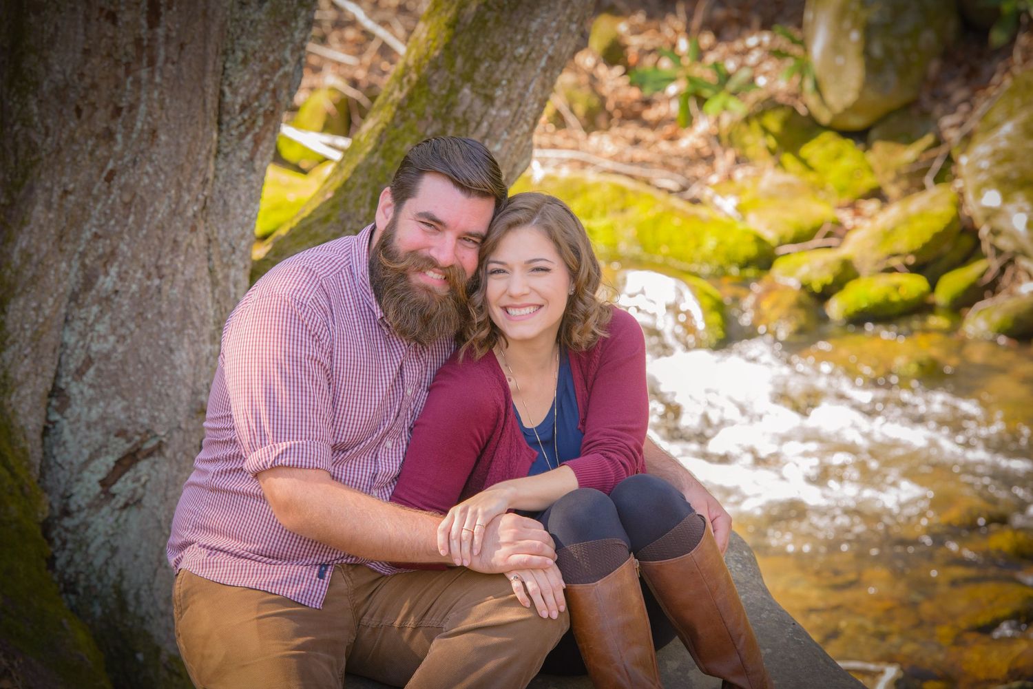 Gatlinburg TN Photographer portrait of a couple sitting together by a tranquil stream with mossy rocks in a romantic outdoor setting.