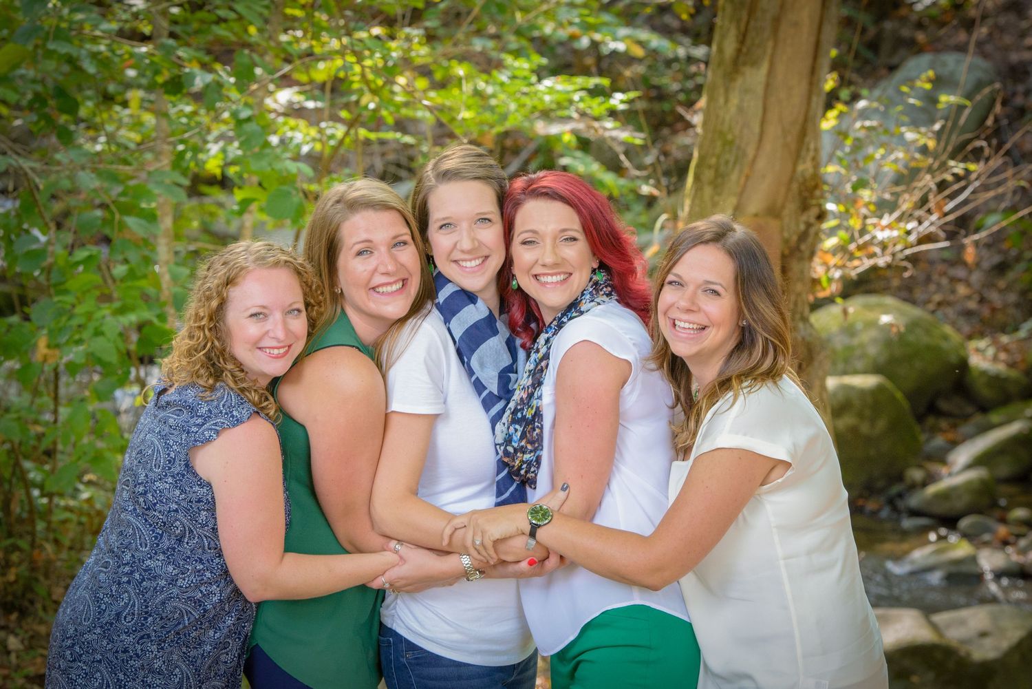 Pigeon Forge Photographer portrait of sisters in coordinated navy and green outfits embrace while posing together by a creek.