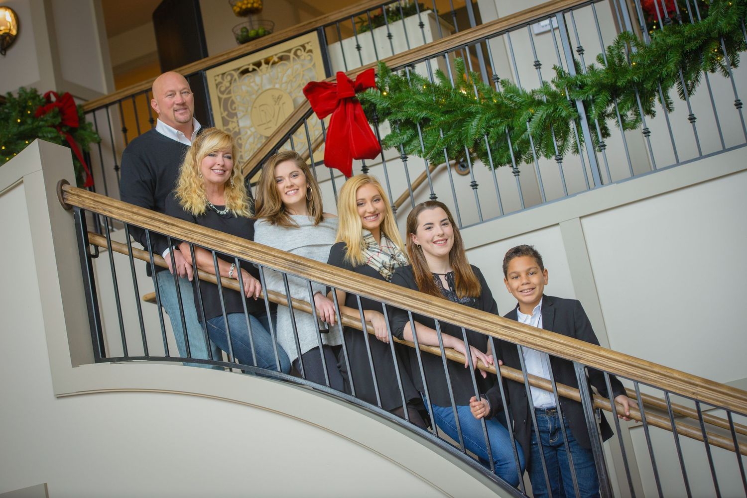 Family posed on a curved staircase decorated with Christmas greenery and a red bow during holiday season at DreamMore Resort.