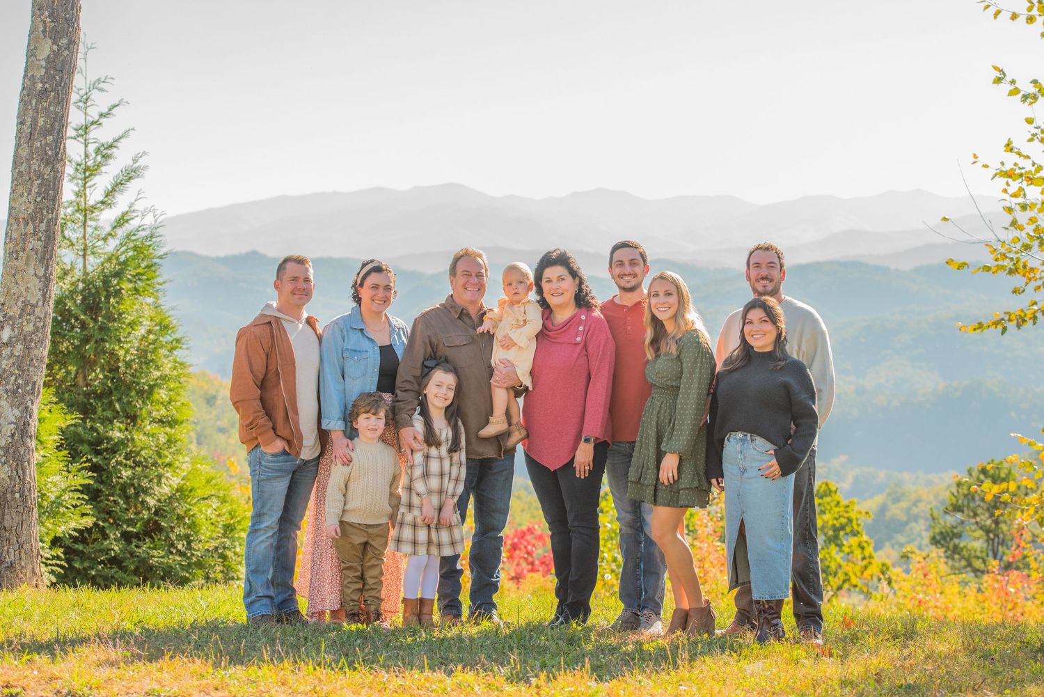 A family poses together on a mountaintop during autumn with colorful foliage and mountain views in the background in Sevierville TN.