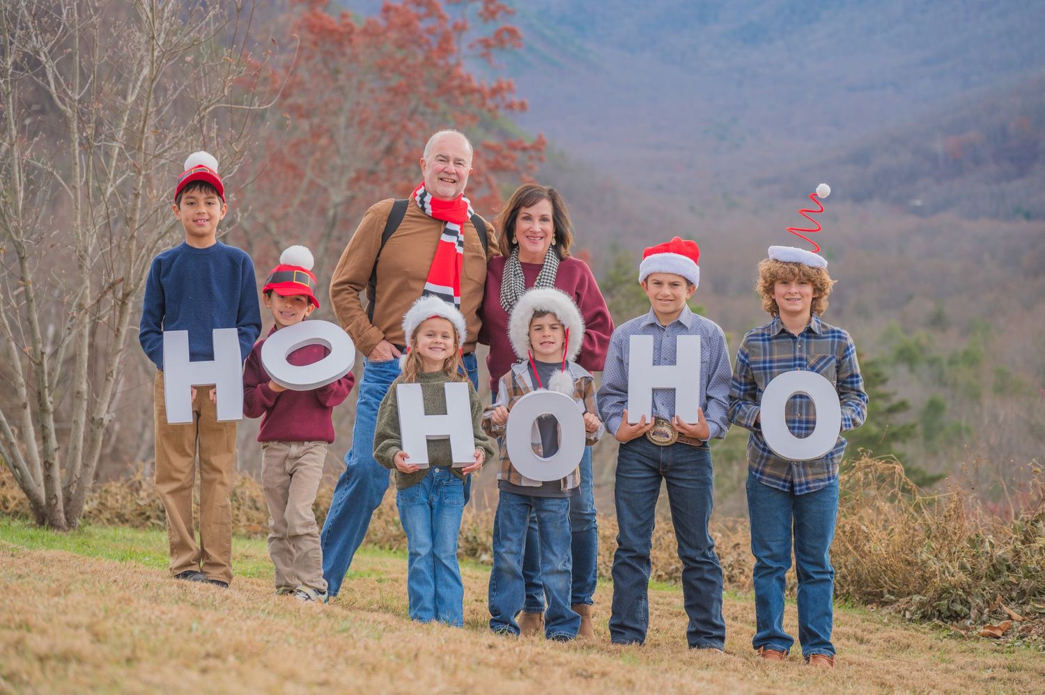 Family wearing Christmas hats and holding H-O-H-O letters stands together on a hillside in autumn by Gatlinburg TN Photographer.