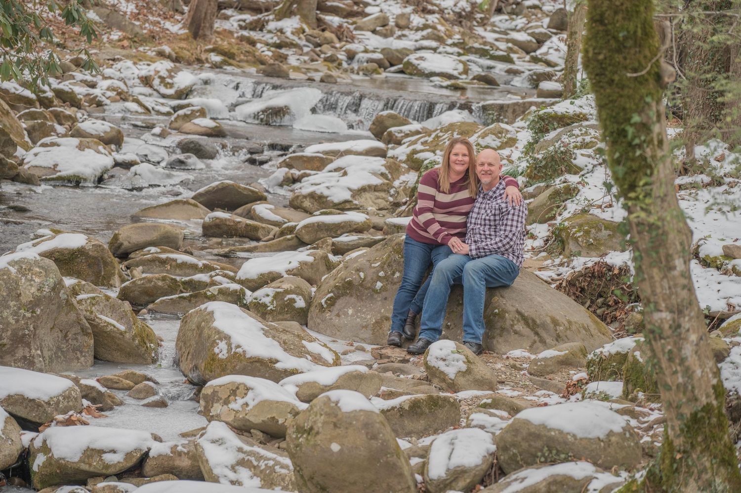 Two people sit together on a rocky outcrop surrounded by snow in a winter forest setting near Pittman Center tn.