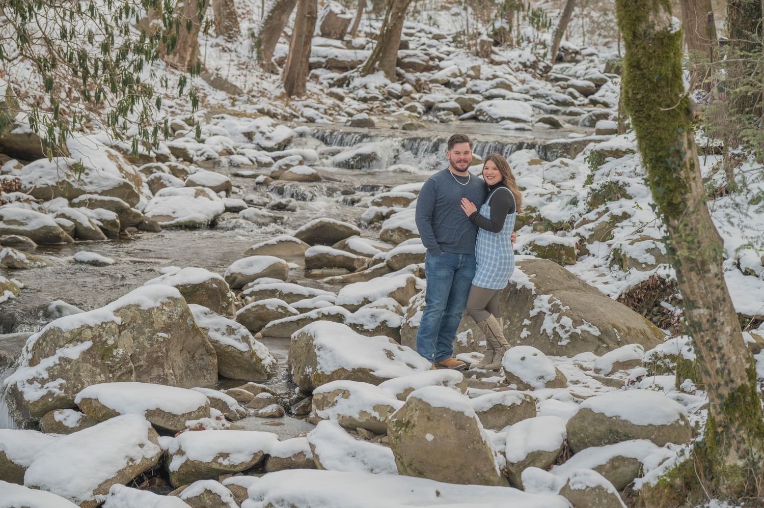 Two people embrace while standing on snow-covered rocks in a winter forest landscape by gatlinburg tn anniversary photographers.