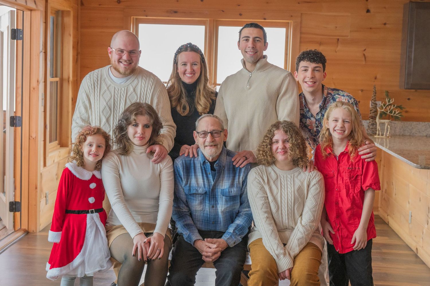 Multi-generational family group poses together in a sunlit wooden cabin hallway at their Gatlinburg cabin rental in TN.