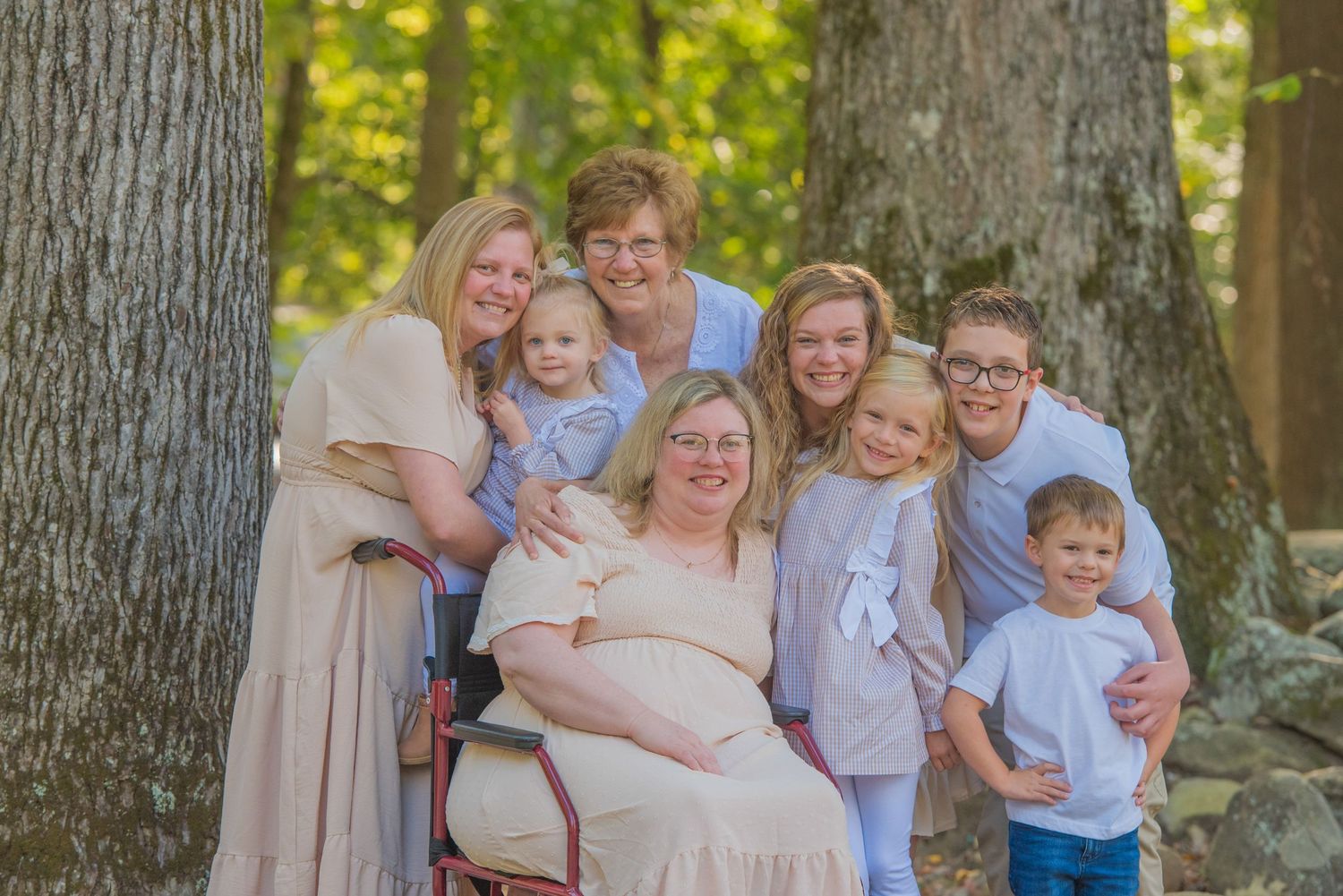 A family group in soft neutral colors poses together in a wooded outdoor setting during a sunny day by Pigeon Forge TN photographers.