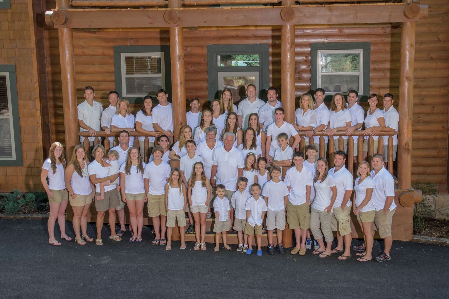 Gatlinburg Photographer portrait of a large group wearing all white clothing poses together on rustic wooden cabin porch for summer photo.