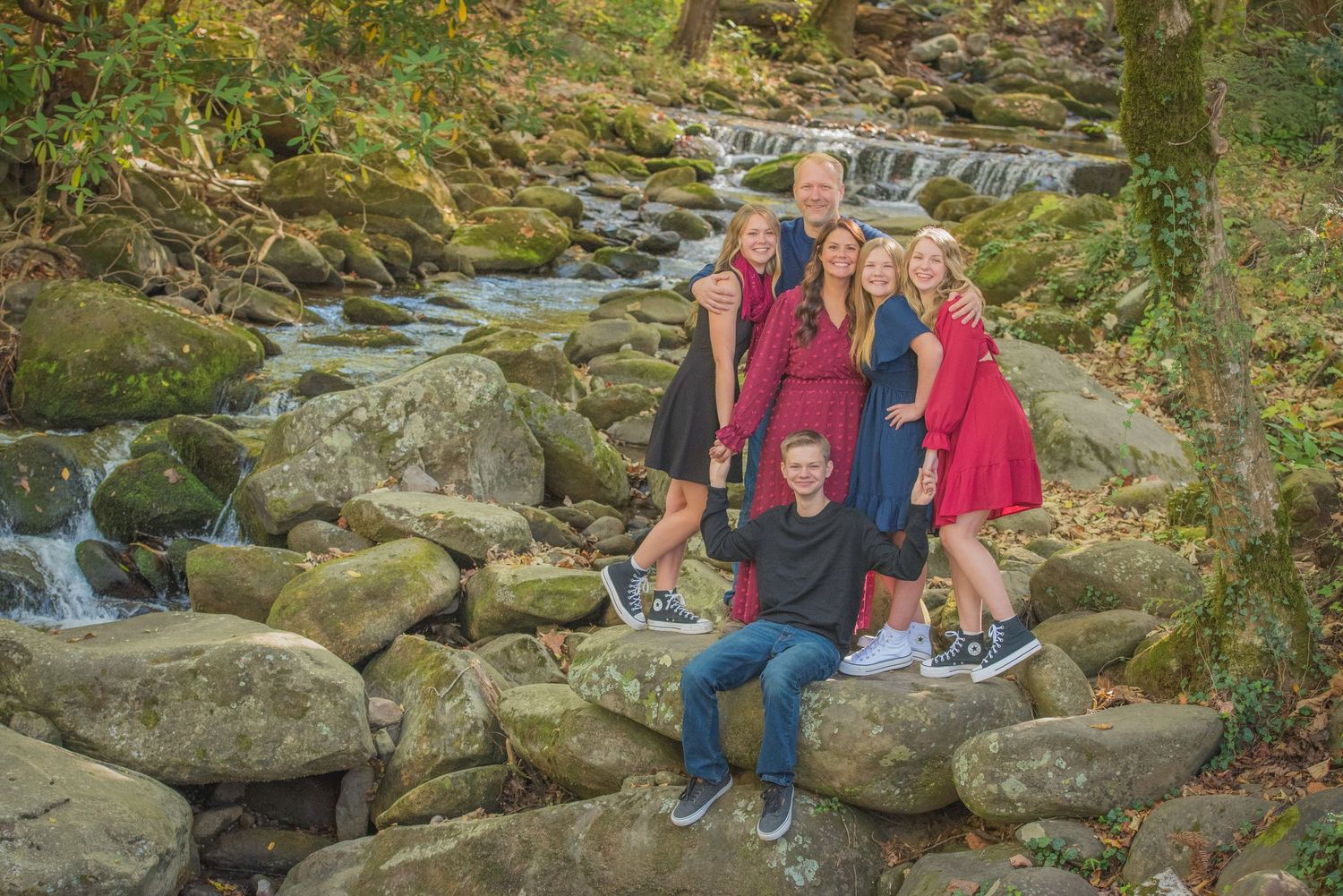 Gatlinburg TN photographers portrait of a family pose together on mossy rocks by a cascading forest stream in autumn.