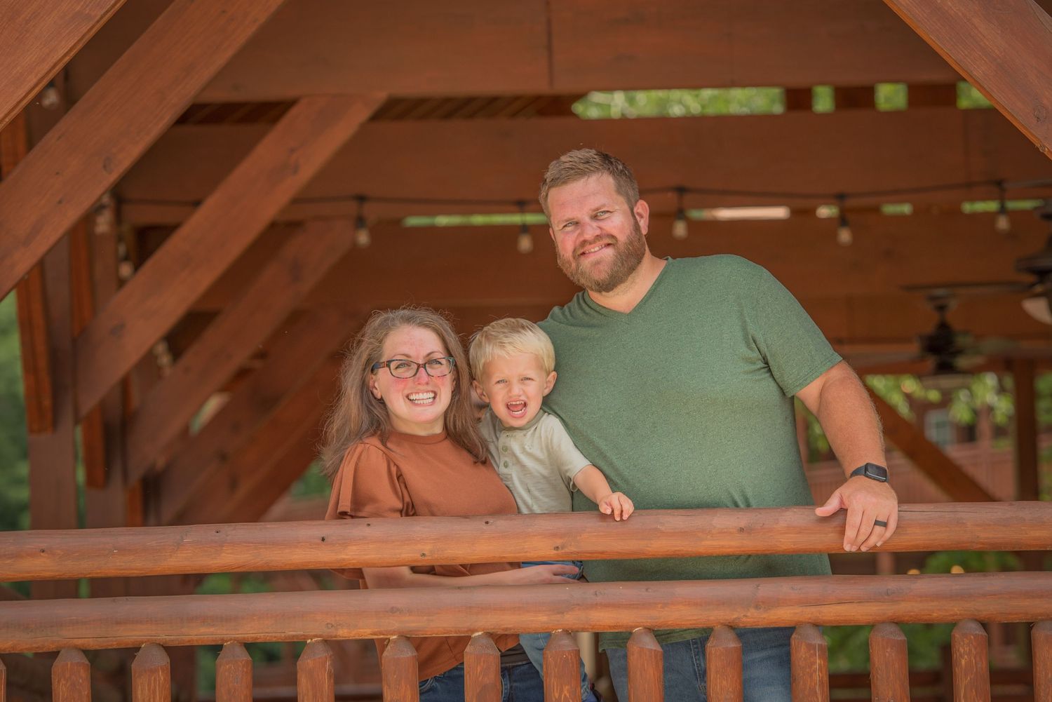 A family smiling together while standing in a wooden gazebo on a warm afternoon by Gatlinburg TN Photographer.