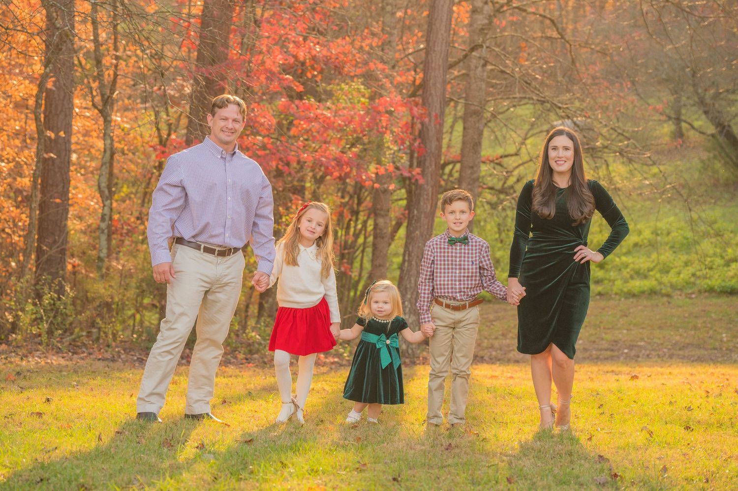 A family group poses together in a scenic autumn forest setting with vibrant orange foliage and golden sunlight in Sevierville TN.