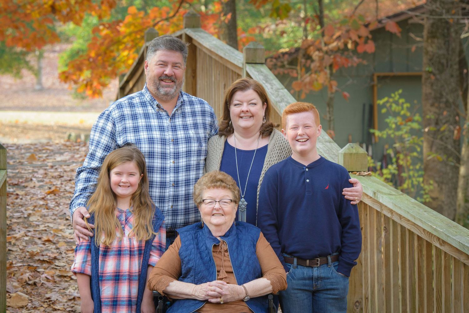 Pigeon Forge photographer outdoor autumn family portrait on wooden deck with colorful fall foliage in background.