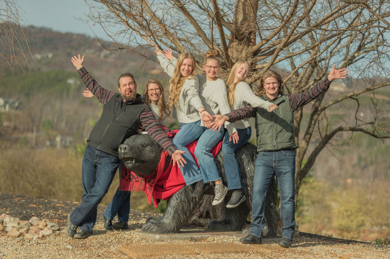 A cheerful group poses energetically together outdoors in front of a bare tree on an autumn day by Gatlinburg Photographer tn.
