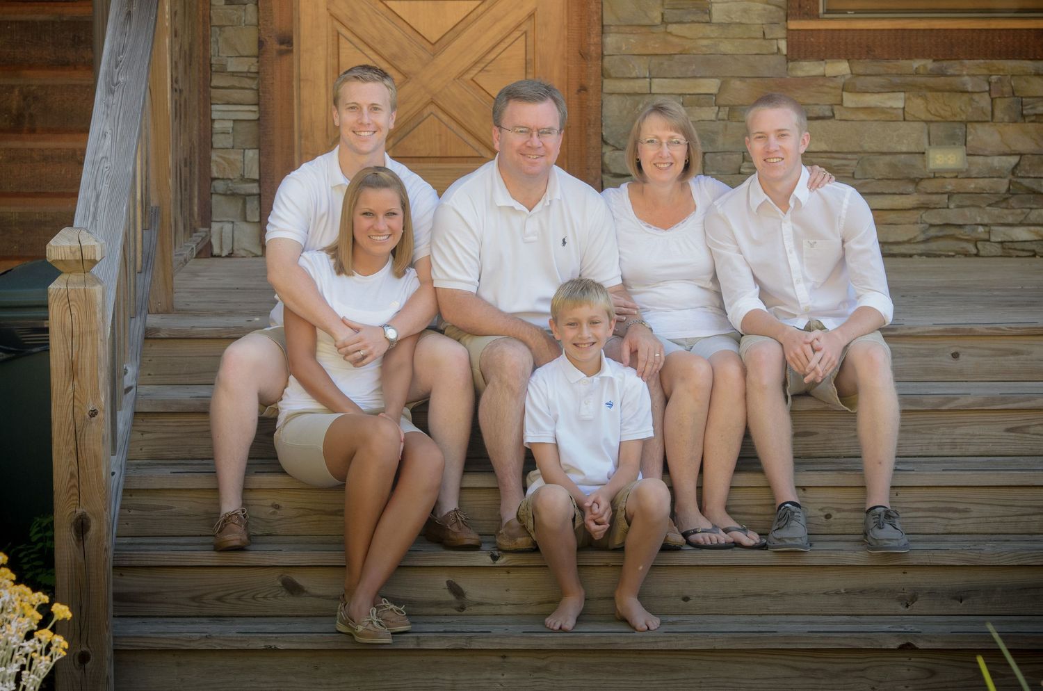 Family group wearing coordinated white and khaki outfits poses together on wooden steps of rustic cabin in Pigeon Forge.