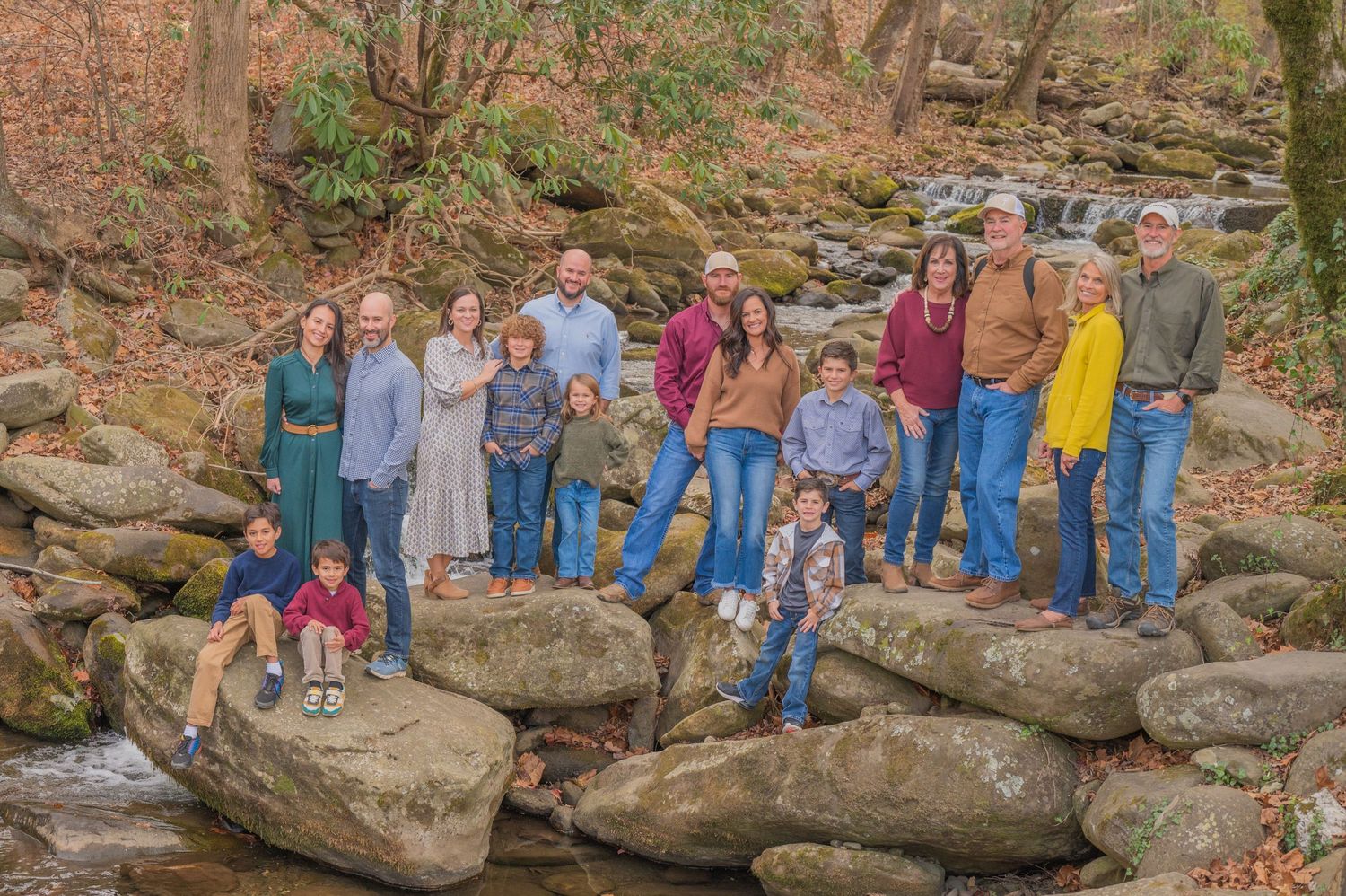 Gatlinburg photographers tn portrait of family posing together on large rocks by a stream in a wooded natural setting during autumn.