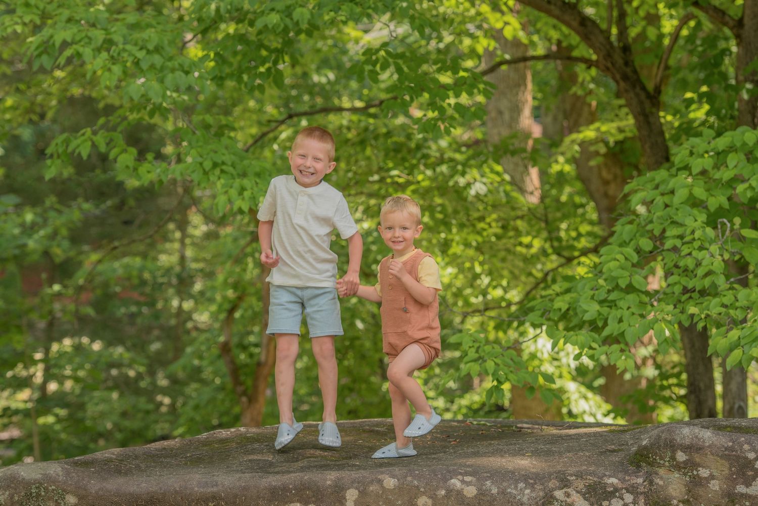 Two children stand together on a large rock in a lush green forest setting during summer Gatlinburg TN.