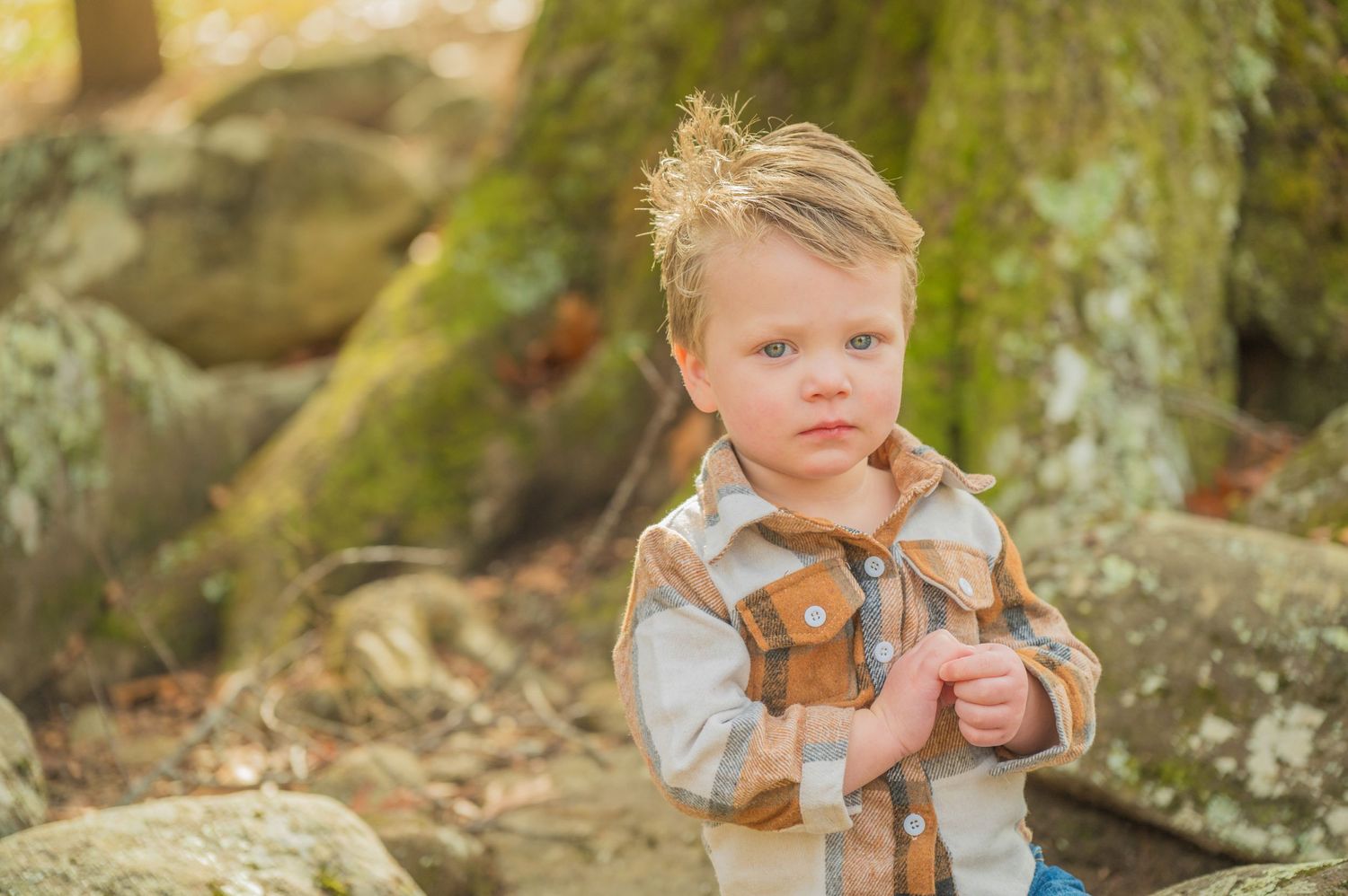 Pigeon Forge Photographer portrait of a young child in rustic outdoor clothing poses among mossy rocks in a natural woodland setting.