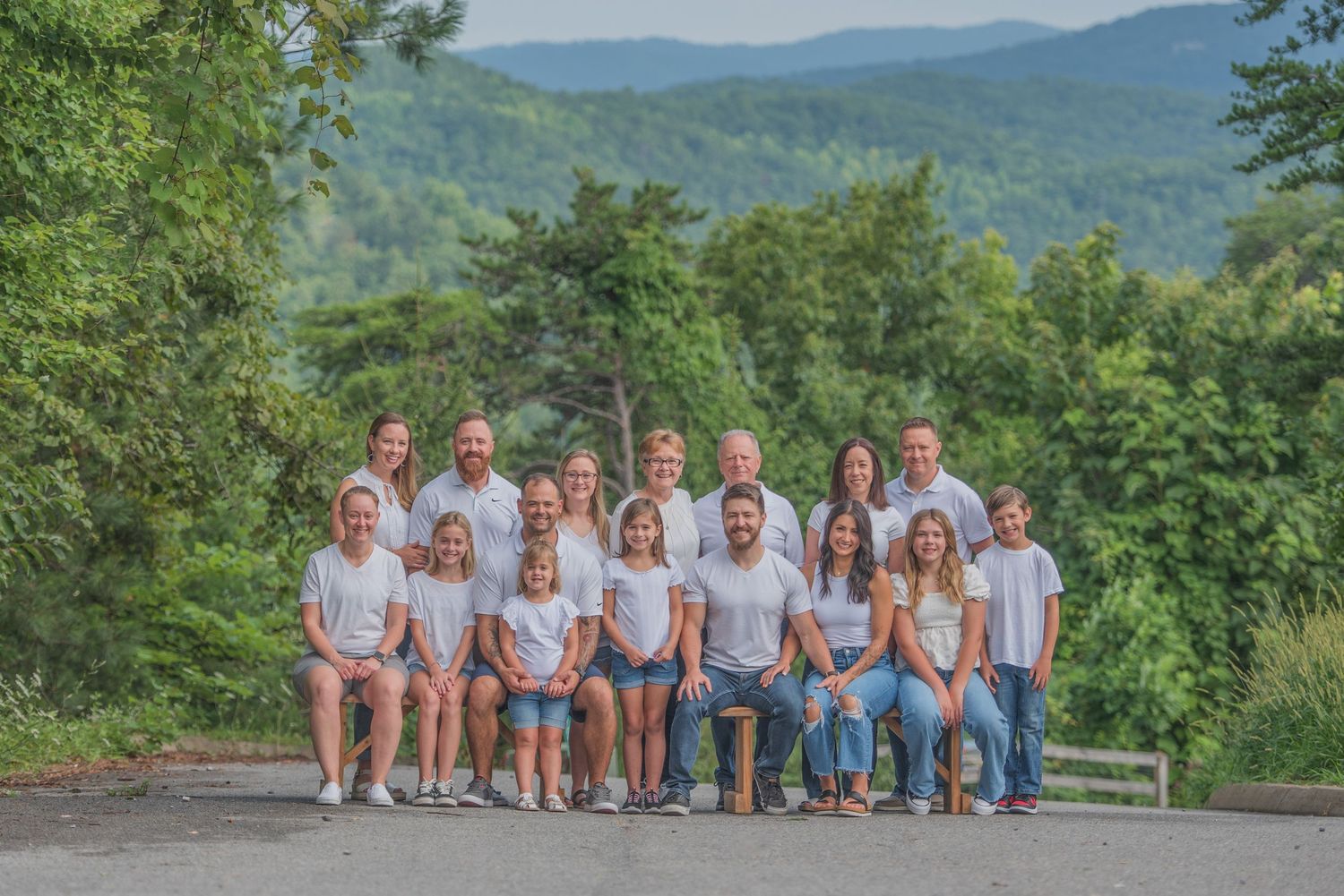 Family dressed in light colored clothing poses together on mountain overlook with green forest and hills in background Pigeon Forge TN.