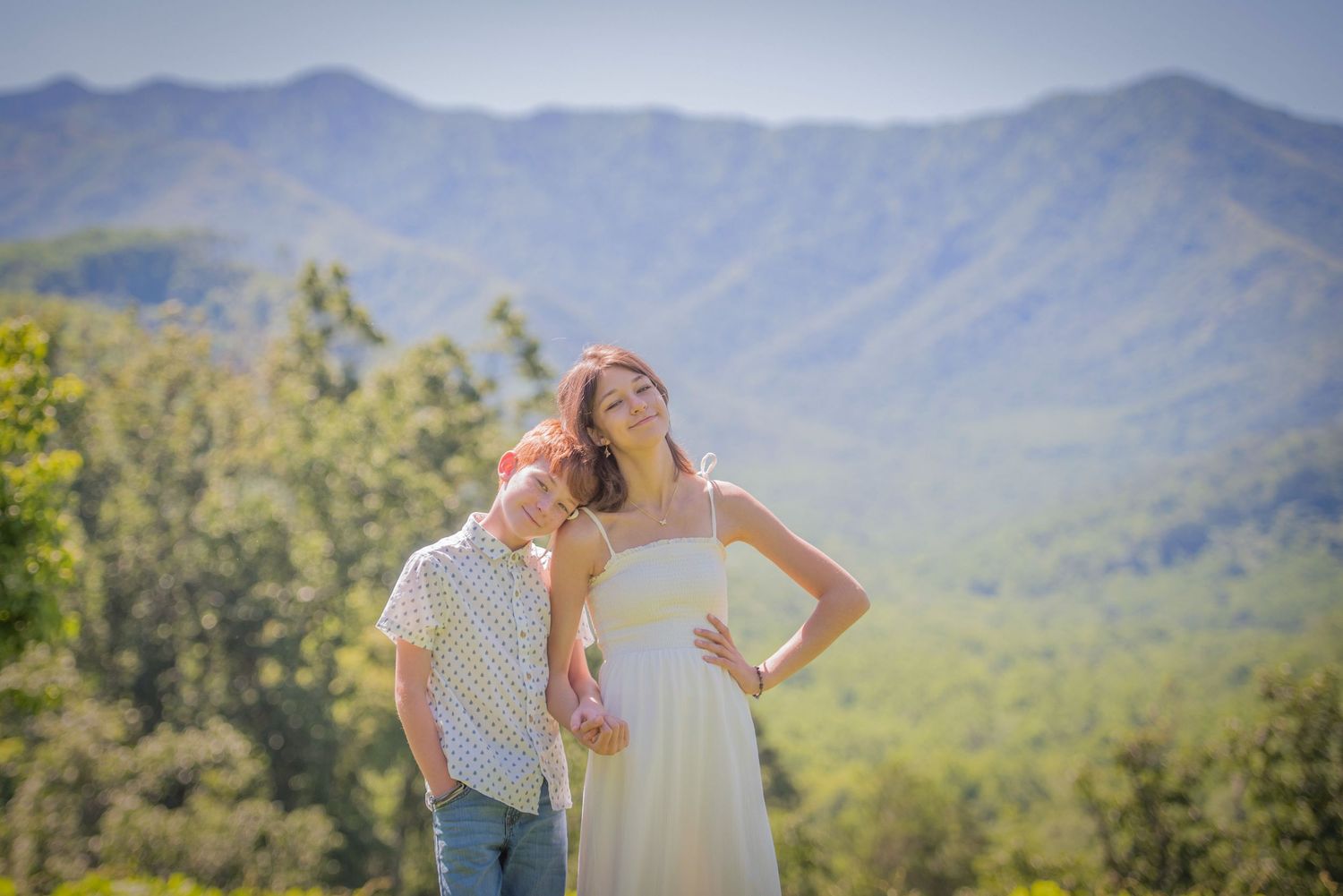 Brother and sister enjoying a scenic mountain vista on a sunny day with lush green valley and rolling peaks in the background Townsend TN.