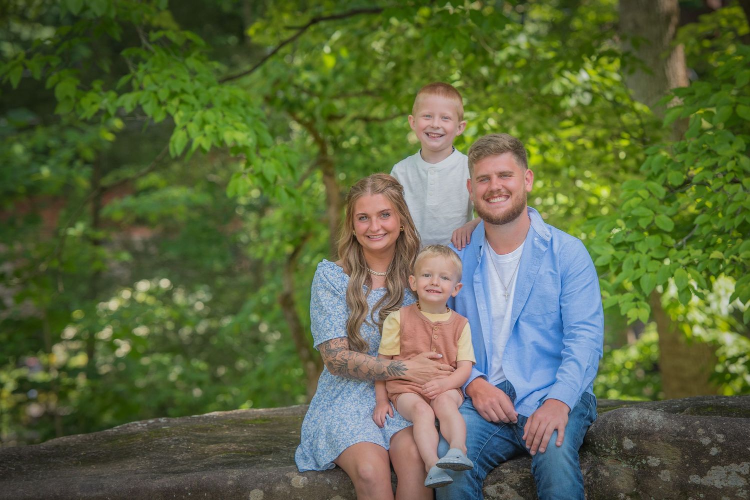 A group poses for a family portrait while sitting together on a wooden surface surrounded by lush green foliage.