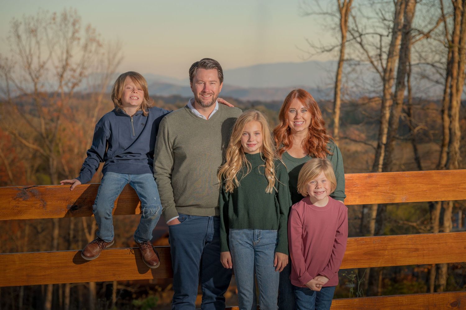 Gatlinburg TN Photographer portrait of a family poses together on a wooden deck railing during golden hour with autumn mountains.