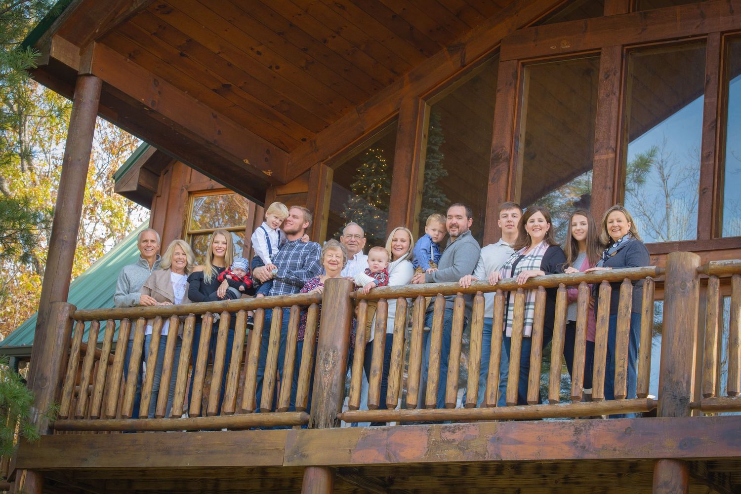 A group stands together on a rustic wooden cabin porch surrounded by autumn foliage at their cabin rental in Sevierville tn.